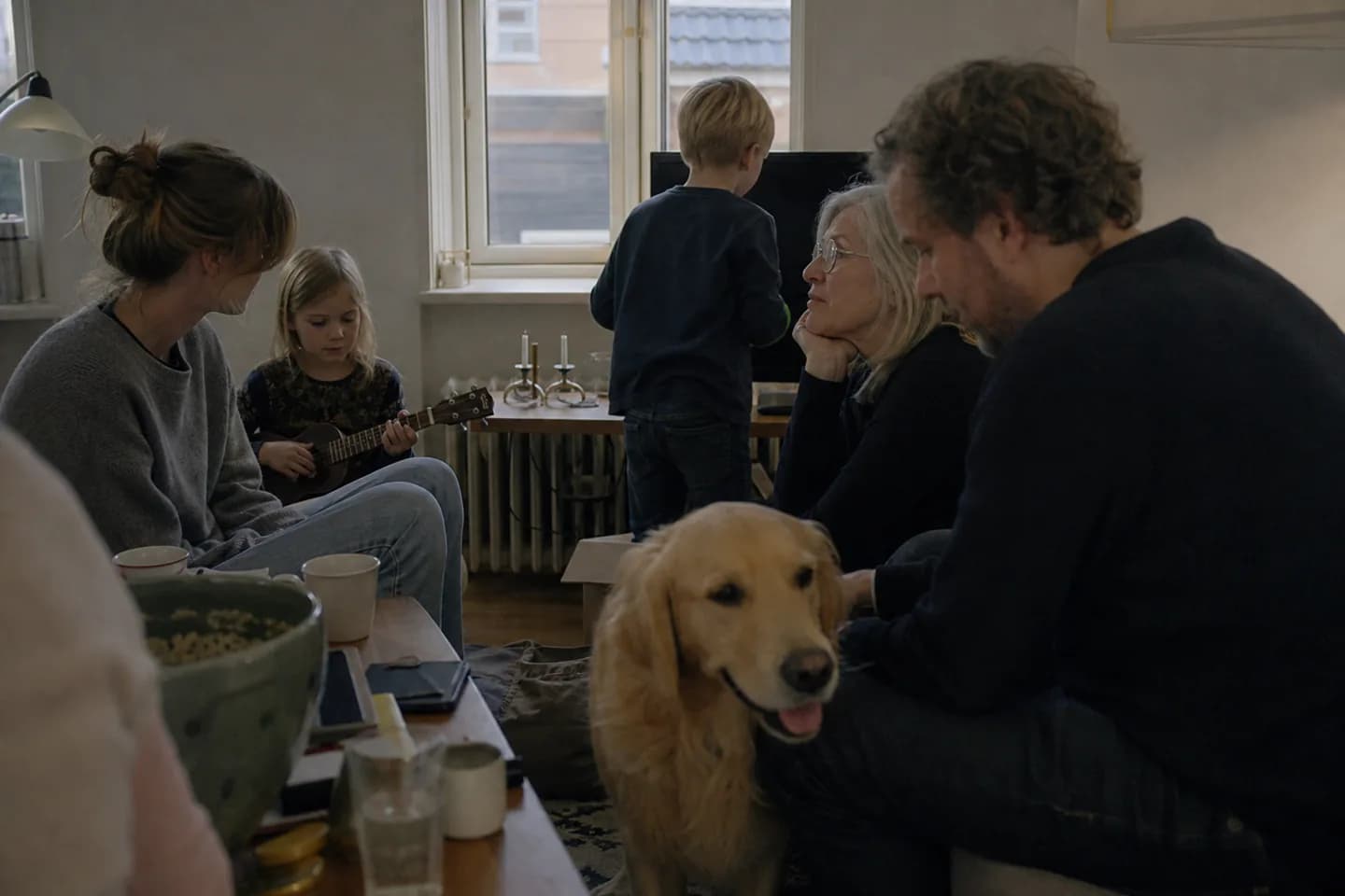 En familie sidder samlet i stuen en aften, hvor golden retrieveren ligger midt i rummet.